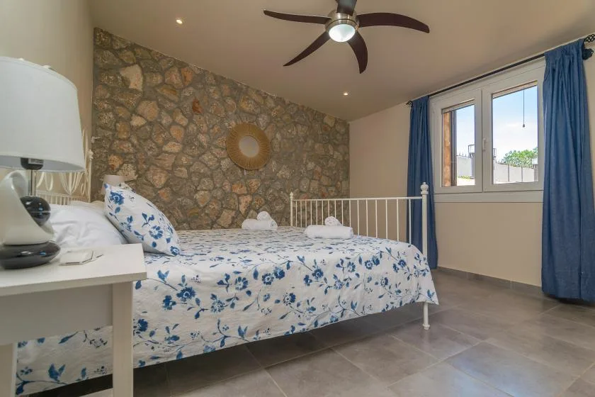 A bedroom with floral bedding, a stone-patterned wall, and a window with blue curtains.