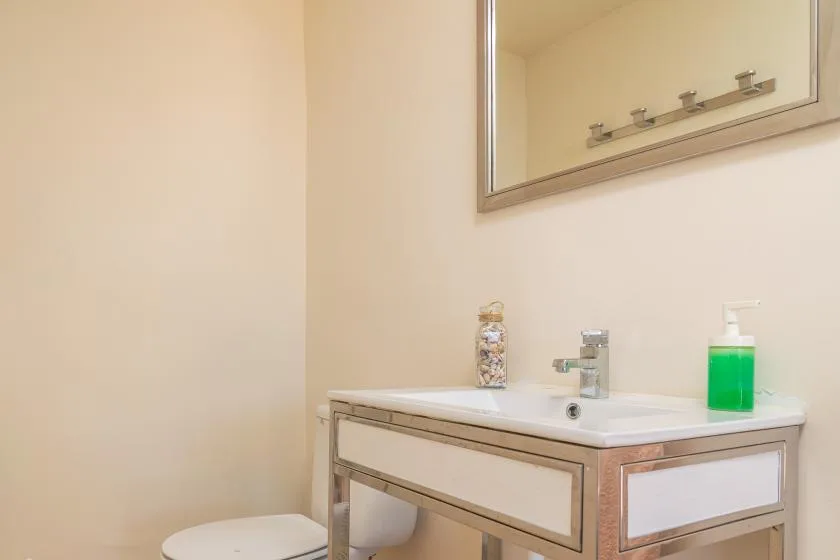 A bathroom vanity with a sink, mirror, and green soap dispenser.