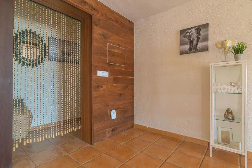 A tiled entryway with a wooden wall, patterned glass door, and display cabinet.