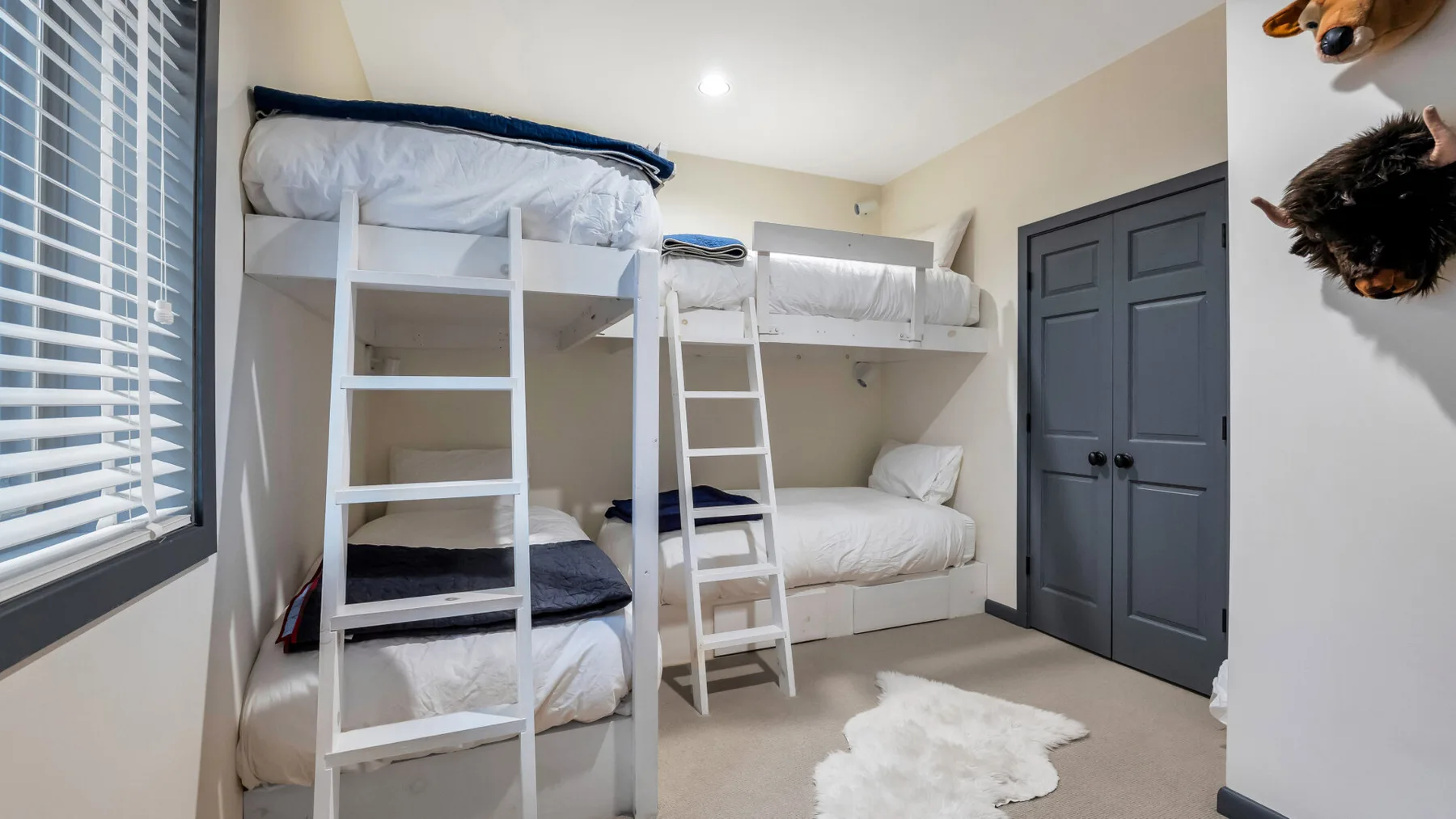 Un dormitorio con literas blancas, una cama inferior y una puerta de armario oscura.