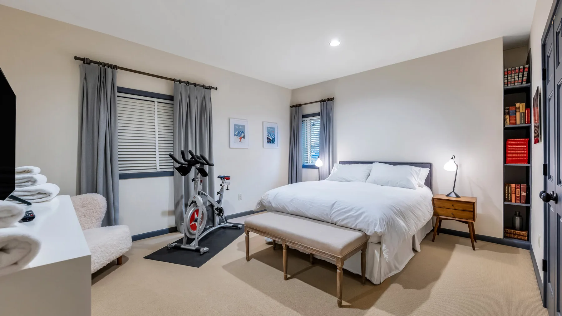 Un dormitorio luminoso con una cama bien arreglada y equipo de ejercicio junto a la ventana.