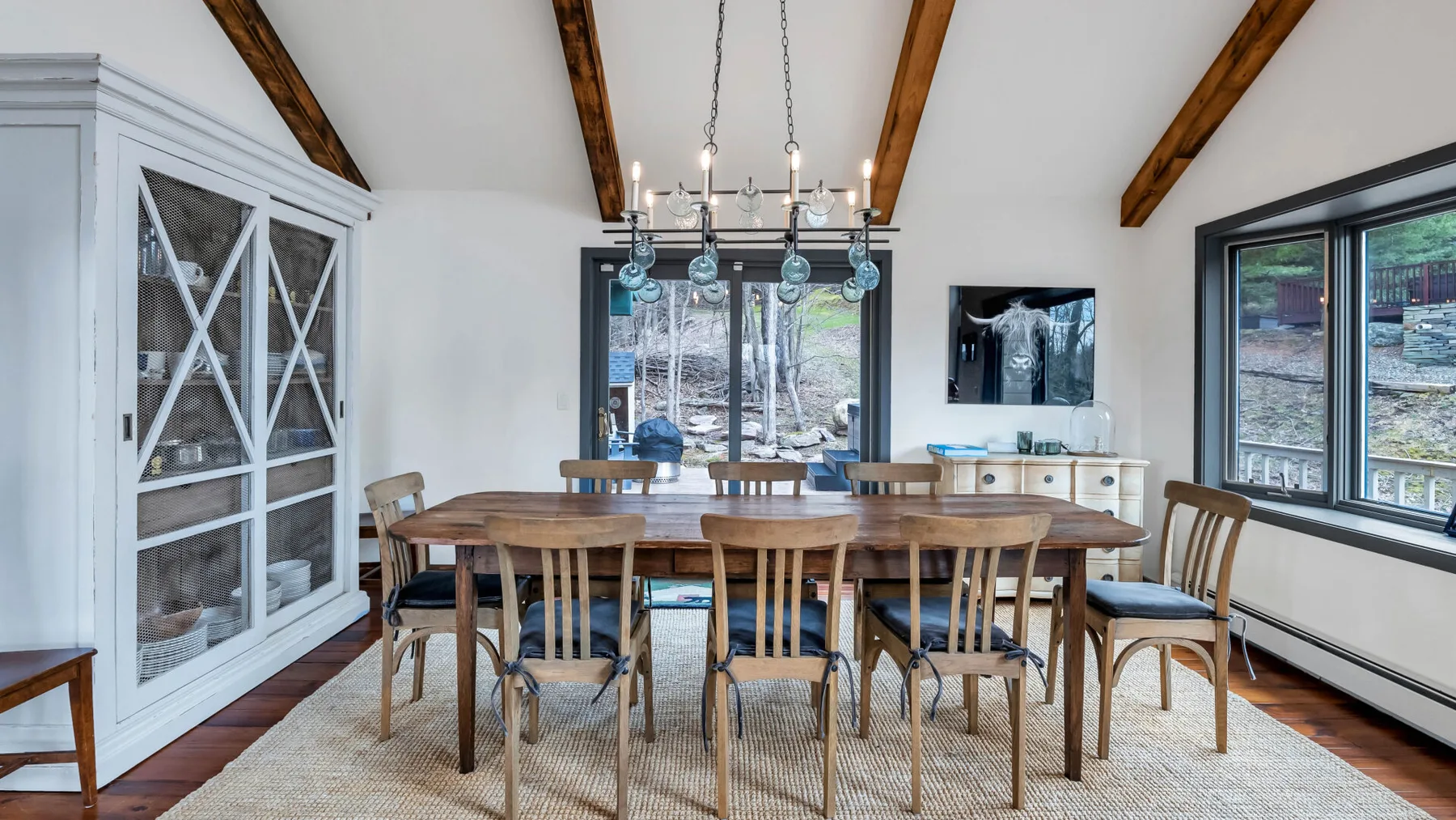 Un comedor luminoso con una mesa larga de madera bajo vigas expuestas.