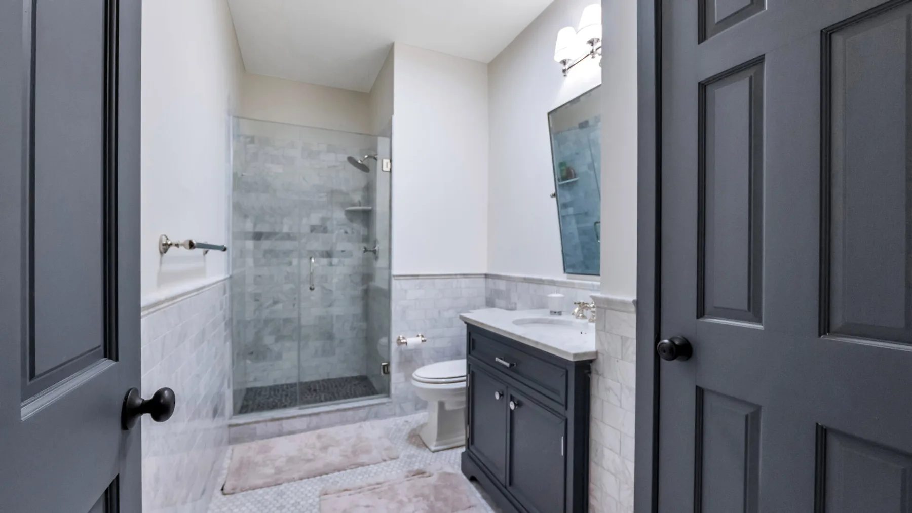 Un baño con ducha de vidrio, inodoro y tocador oscuro.
