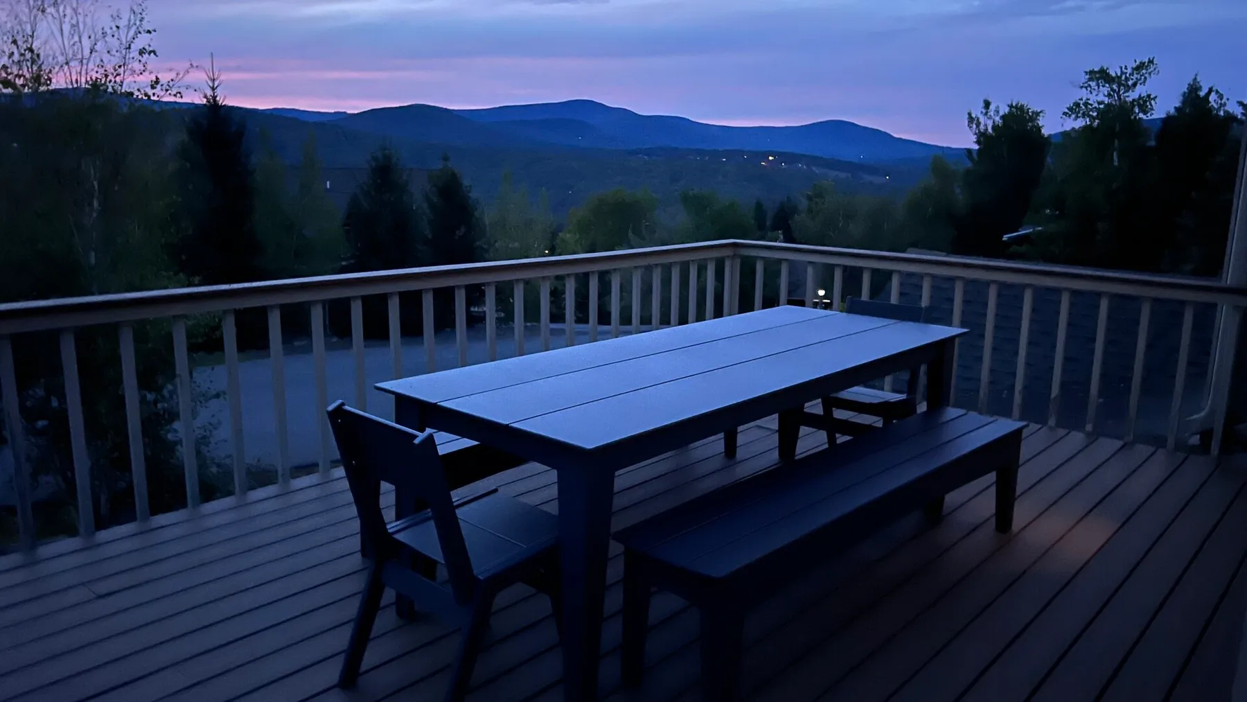 Una terraza con una mesa de picnic ofrece vistas de colinas boscosas al anochecer.