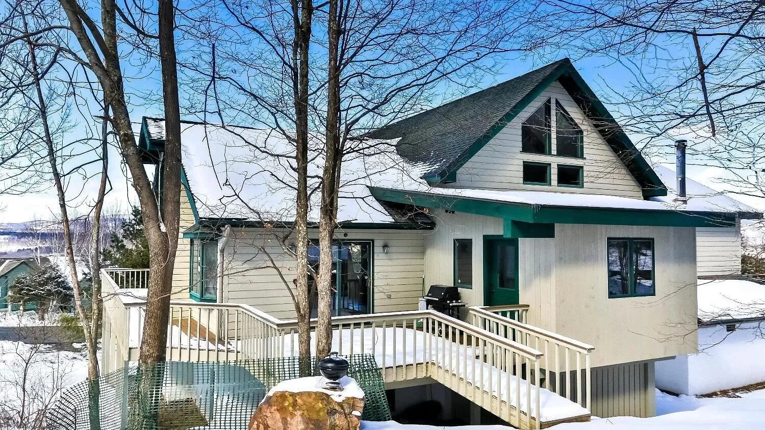Una casa cubierta de nieve con una terraza elevada de madera y árboles sin hojas.