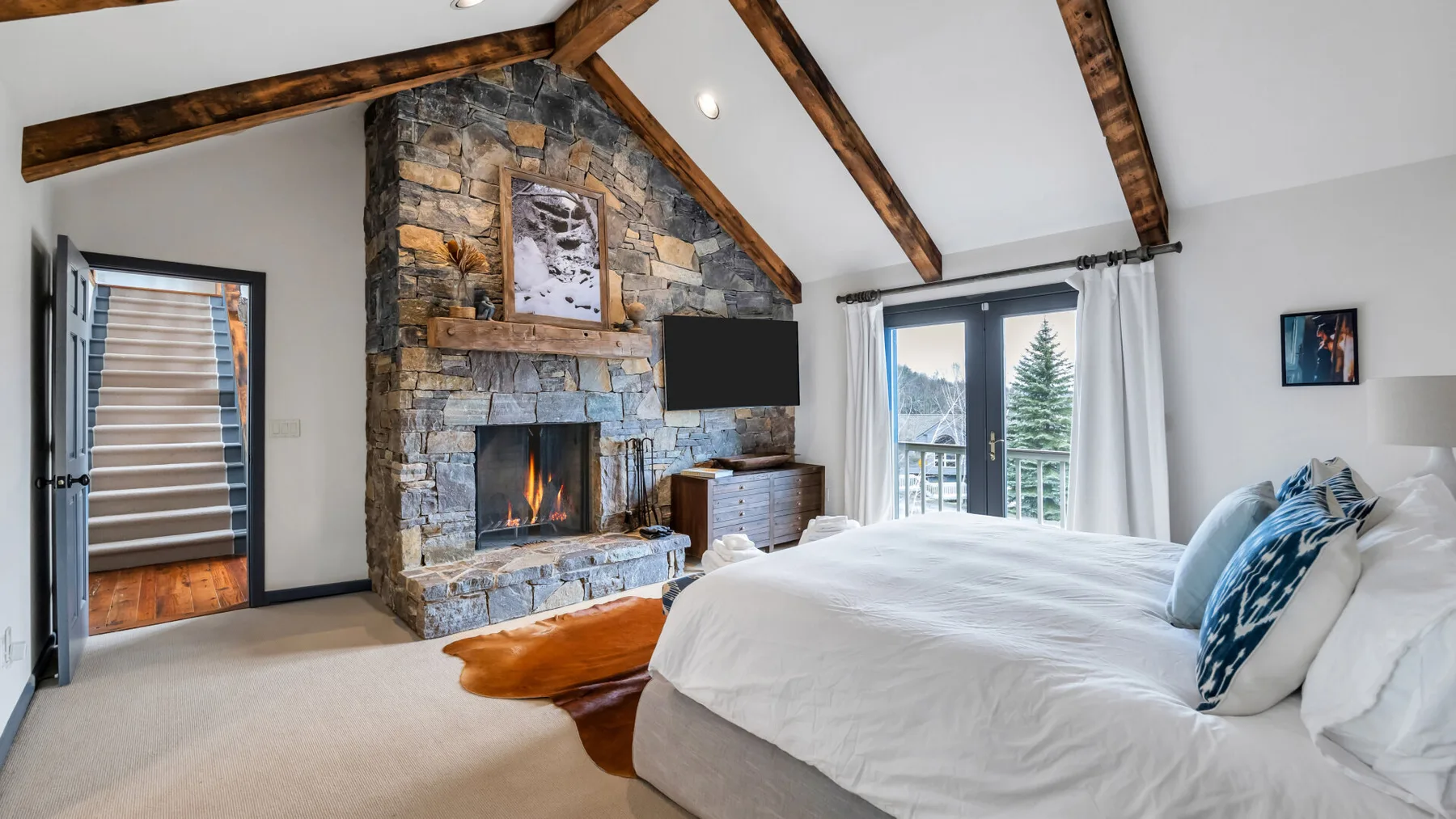 Un dormitorio con una cama grande, una chimenea de piedra y vigas expuestas en el techo.