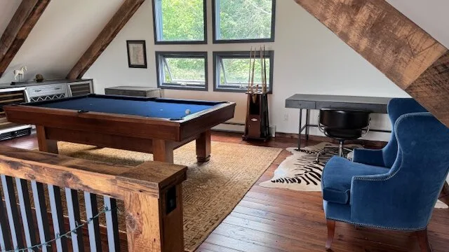 Una sala de juegos con mesa de billar, asientos azules y ventanas grandes.