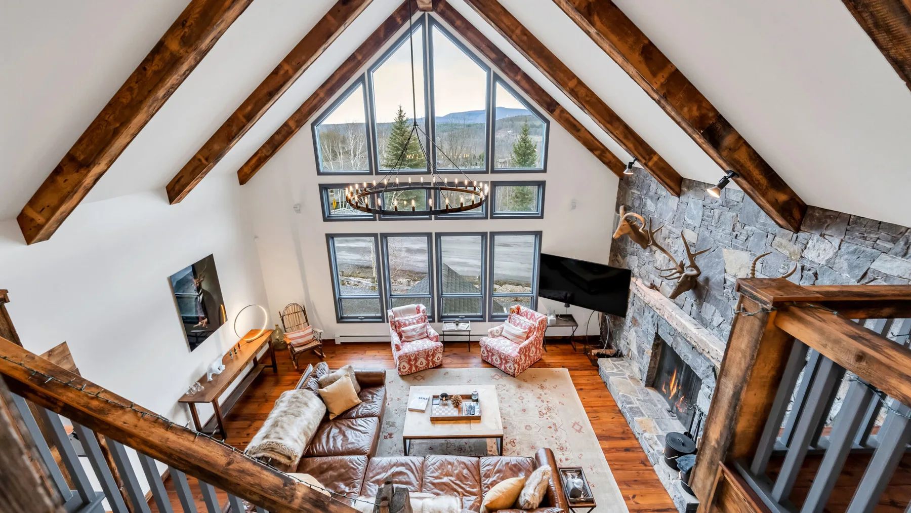 A vaulted living room with exposed wooden beams, seating, and a stone fireplace.