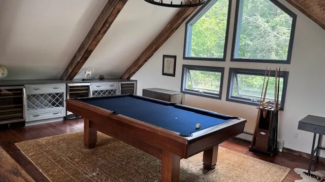 Una sala de billar con una mesa bajo grandes ventanas inclinadas.