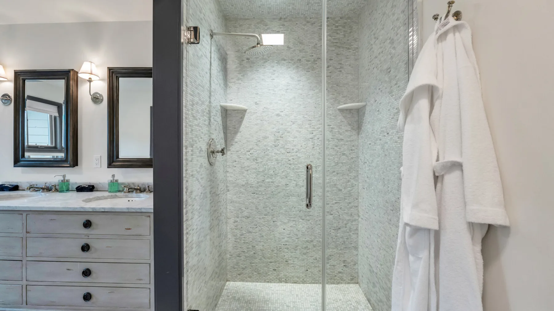 Un tocador de baño y espejos están junto a una ducha con mampara de vidrio.