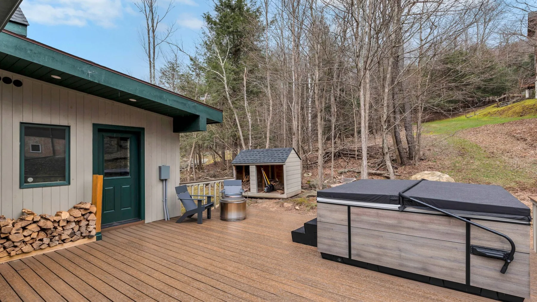 An outdoor deck with a covered hot tub beside a wooded hillside.