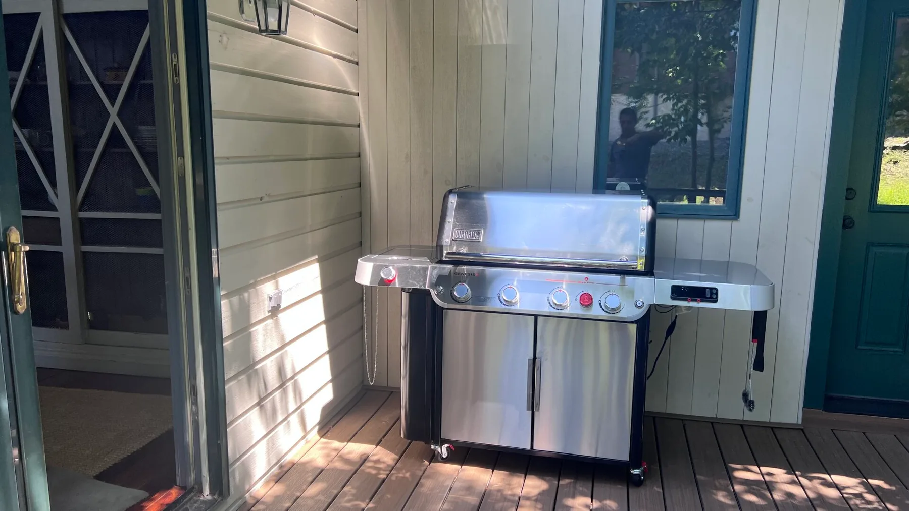 Una parrilla de acero inoxidable está en un porche cubierto junto a una puerta oscura.