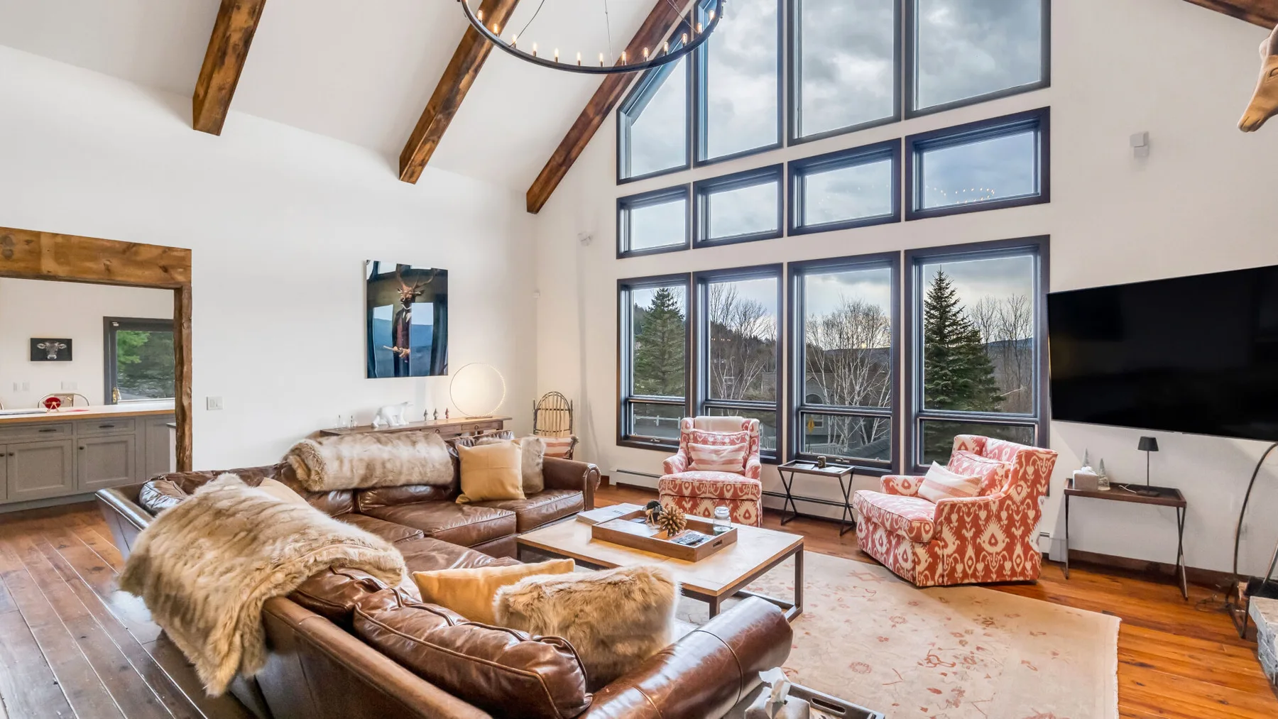 A bright living room with large windows, seating, and a wall-mounted television.