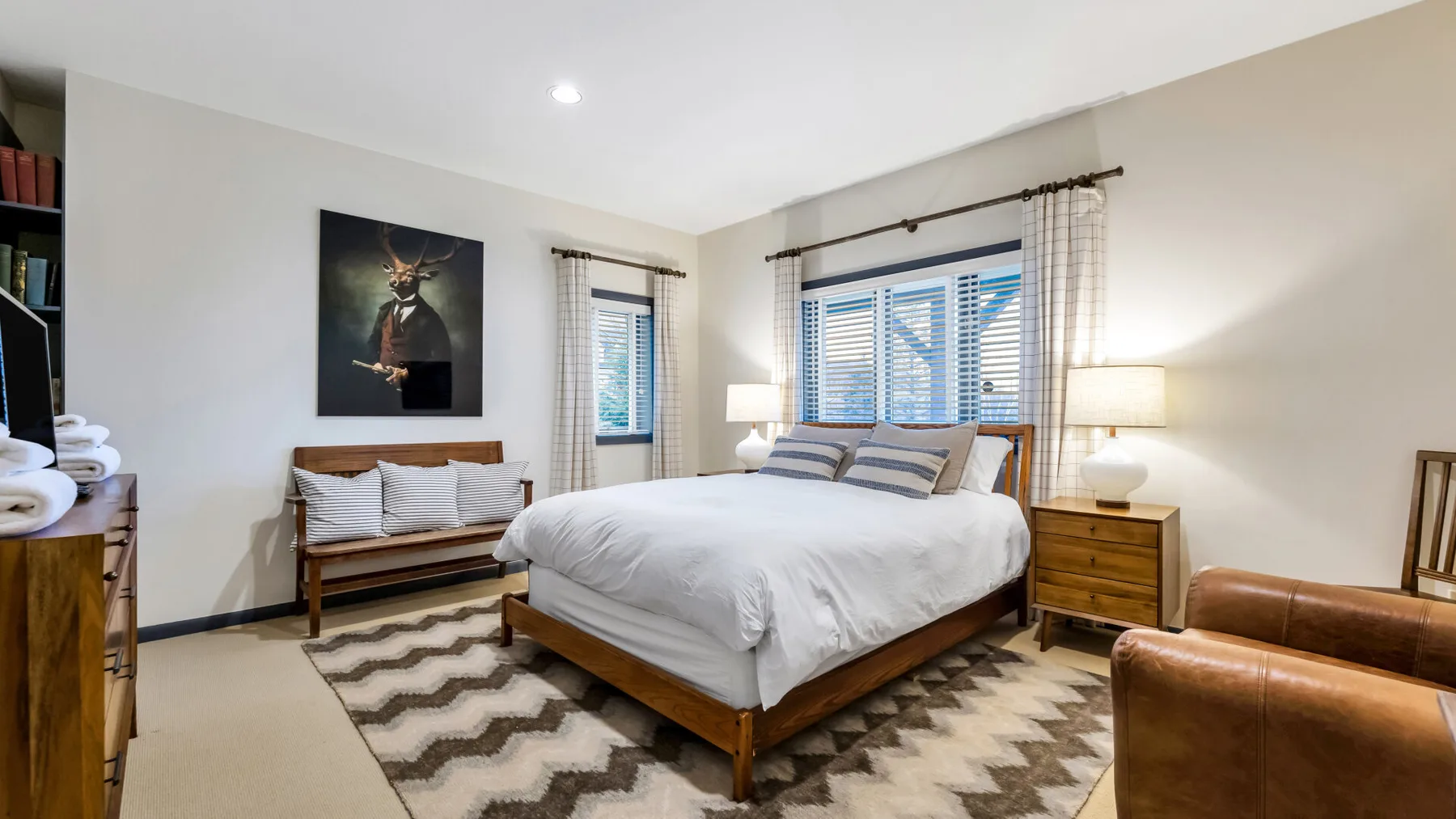 Un dormitorio con una cama, mesitas de madera y ventanas con persianas.