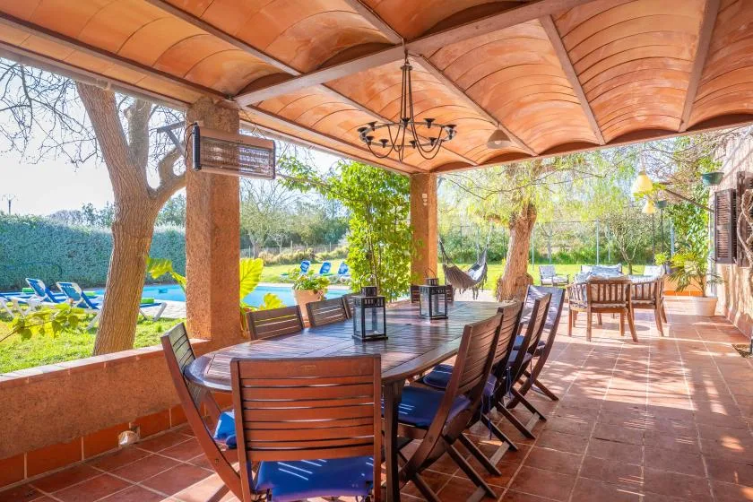 Un comedor exterior cubierto con asientos de madera y una mesa frente a un jardín.
