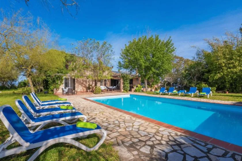 Una piscina al aire libre junto a un patio de piedra, con asientos y árboles.