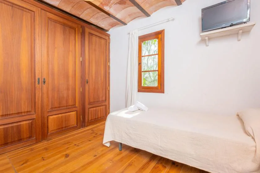 Un dormitorio con un armario de madera, una cama y una ventana.