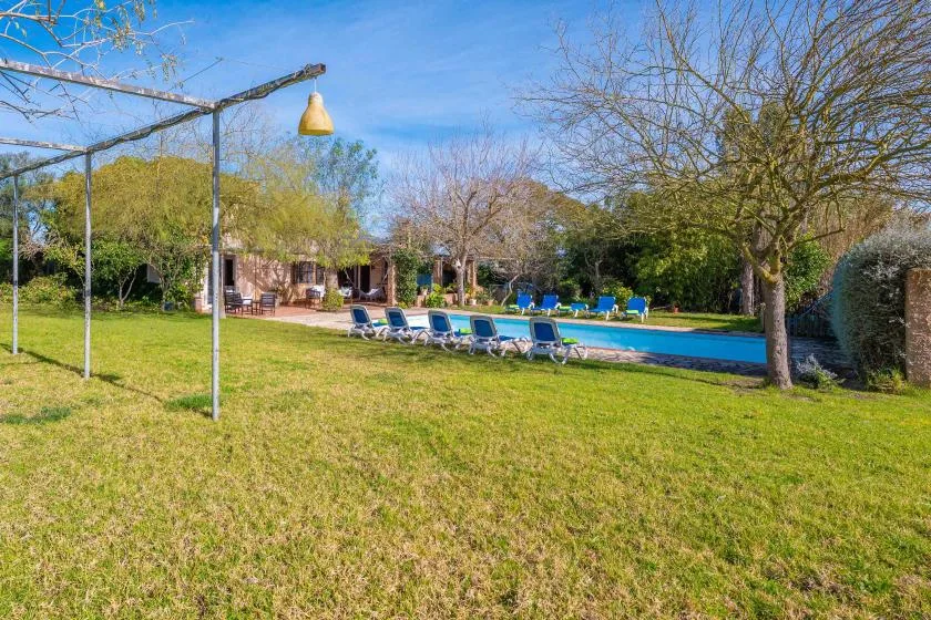 Un jardín con césped rodea una piscina exterior con tumbonas cerca.