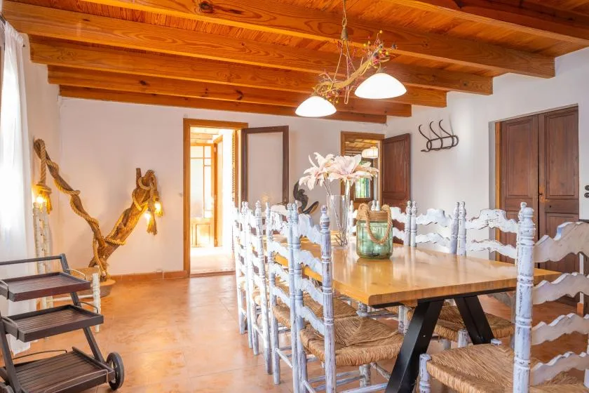 Comedor con una mesa larga de madera y filas de sillas bajo vigas expuestas.