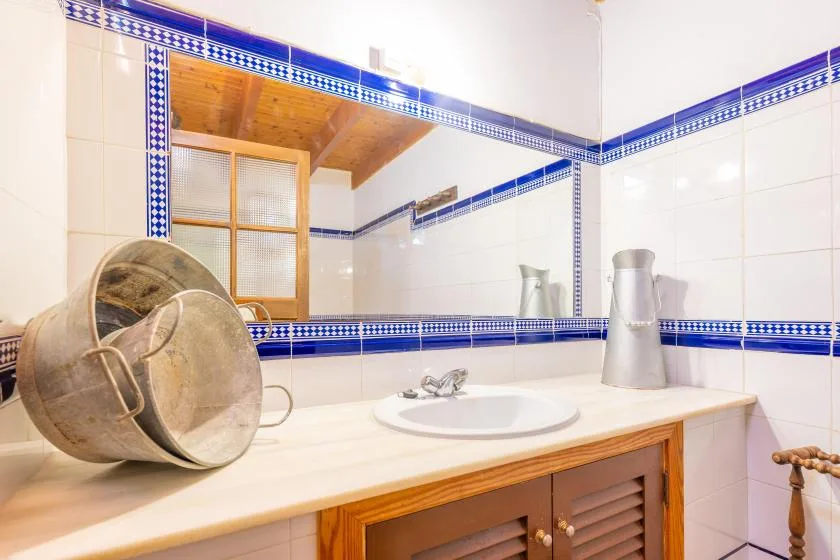 Un tocador de baño alicatado con lavabo, recipientes metálicos y una ventana de madera.