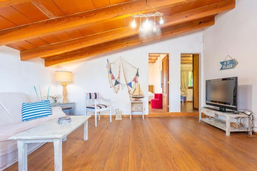 Sala de estar con asientos, un televisor y vigas de madera expuestas en el techo.
