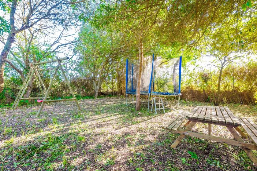 Una zona de juegos al aire libre y sombreada tiene un columpio y un trampolín entre árboles.