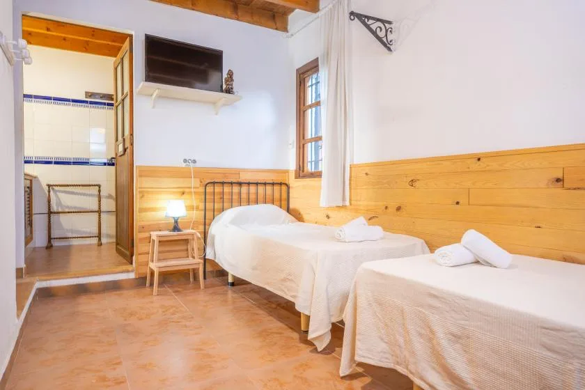 Un dormitorio con dos camas individuales, paneles de madera en la pared y una puerta abierta a un baño alicatado.