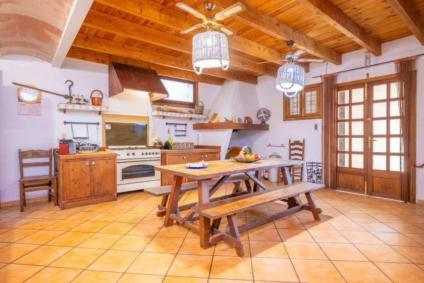 Una cocina y comedor rústicos con una larga mesa de madera bajo vigas vistas.
