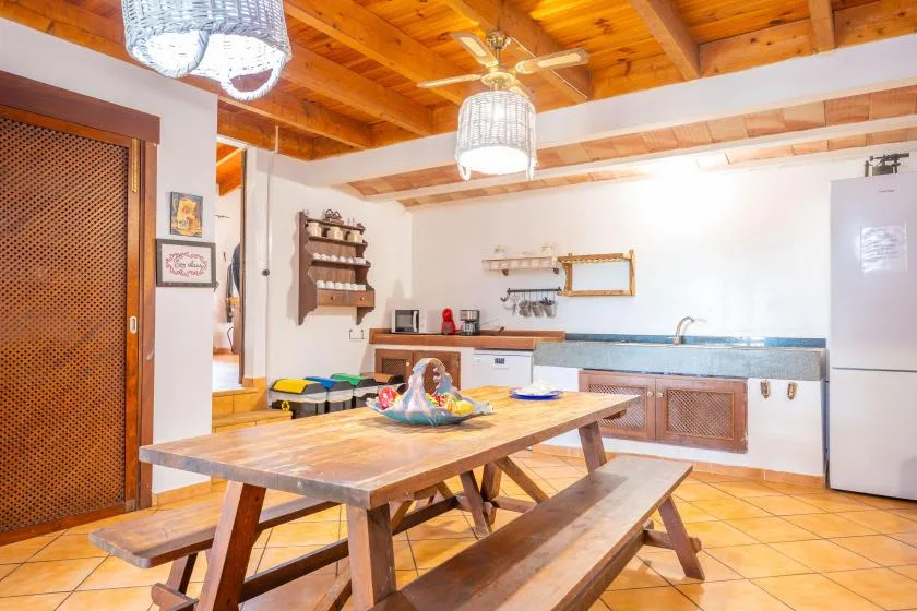 Una cocina luminosa con zona de comedor y una mesa de madera bajo un techo de madera.