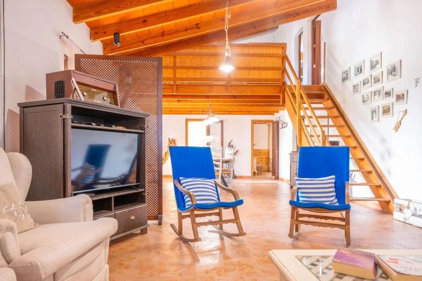 Una sala luminosa con sillones azules y una escalera de madera.