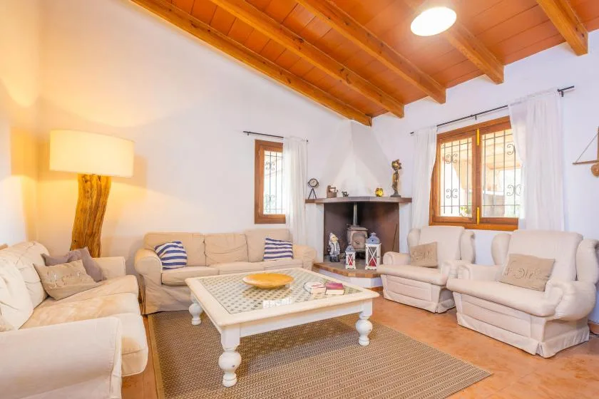Una sala luminosa con asientos claros, una mesa de centro y vigas de madera a la vista.