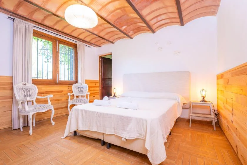 Un dormitorio con una cama grande, paneles de madera y dos sillas junto a la ventana.
