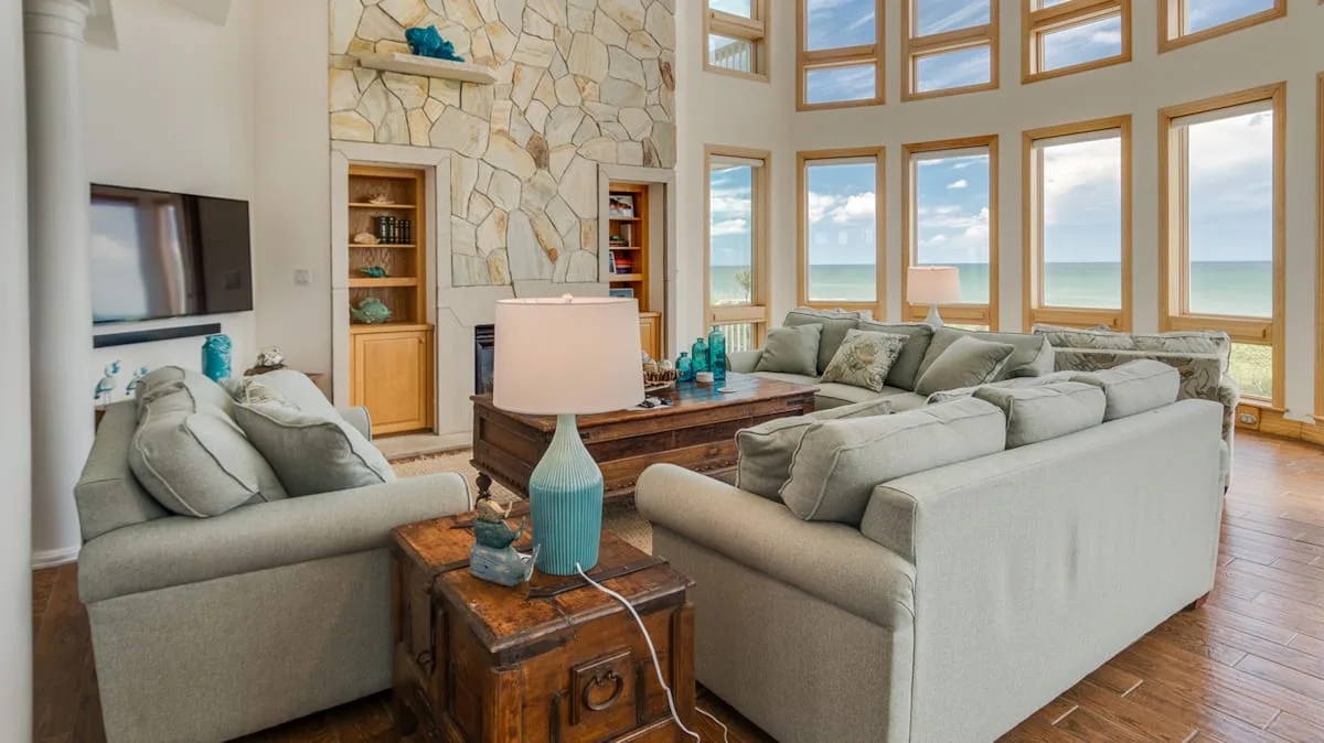 A living room with seating arranged around a wooden coffee table, facing large windows.