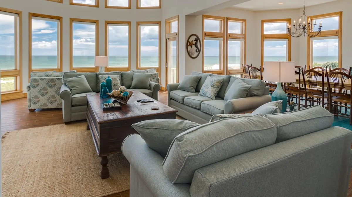 A living room with seating arranged around a coffee table and large windows.
