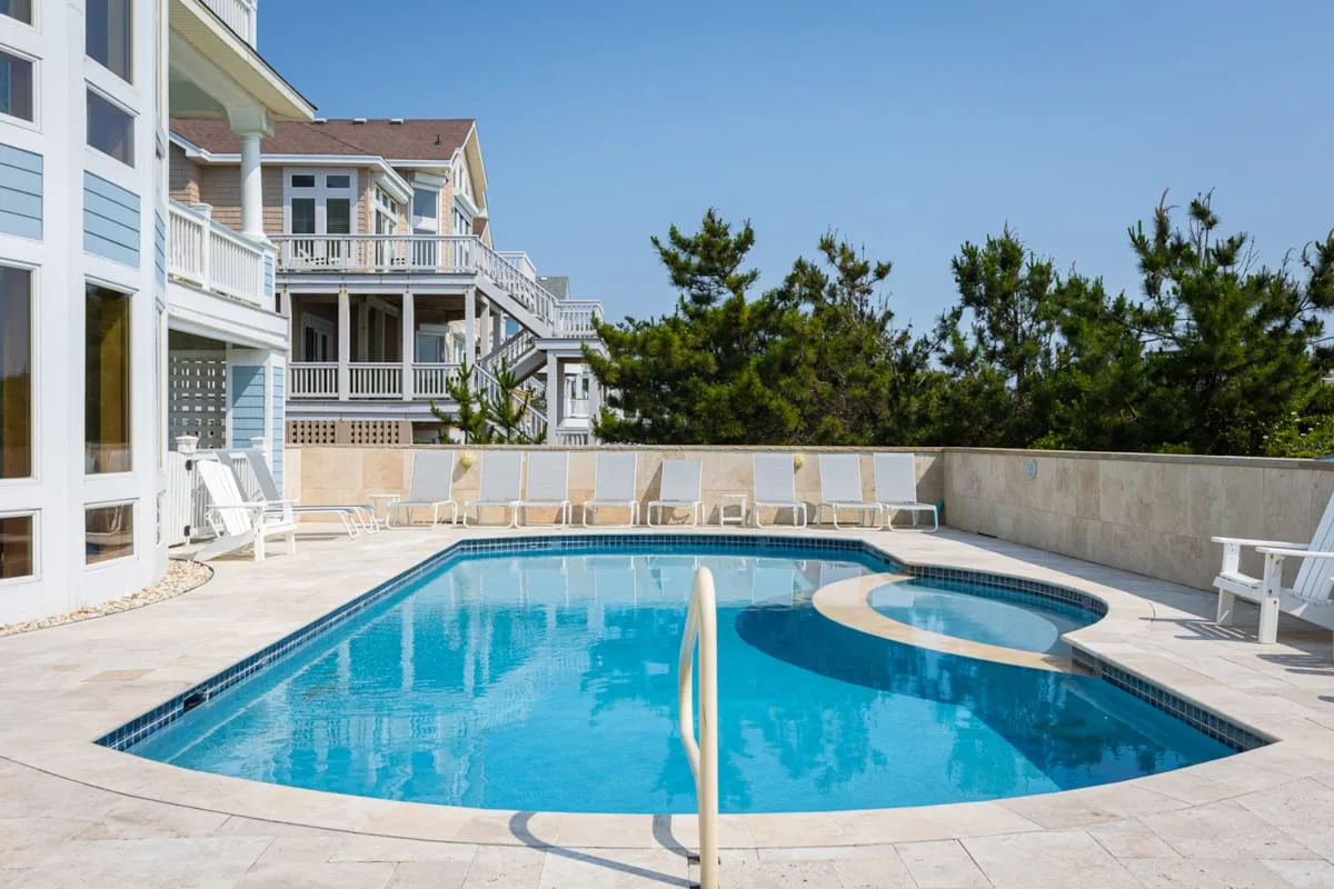 An outdoor swimming pool beside a house, with trees in the background.
