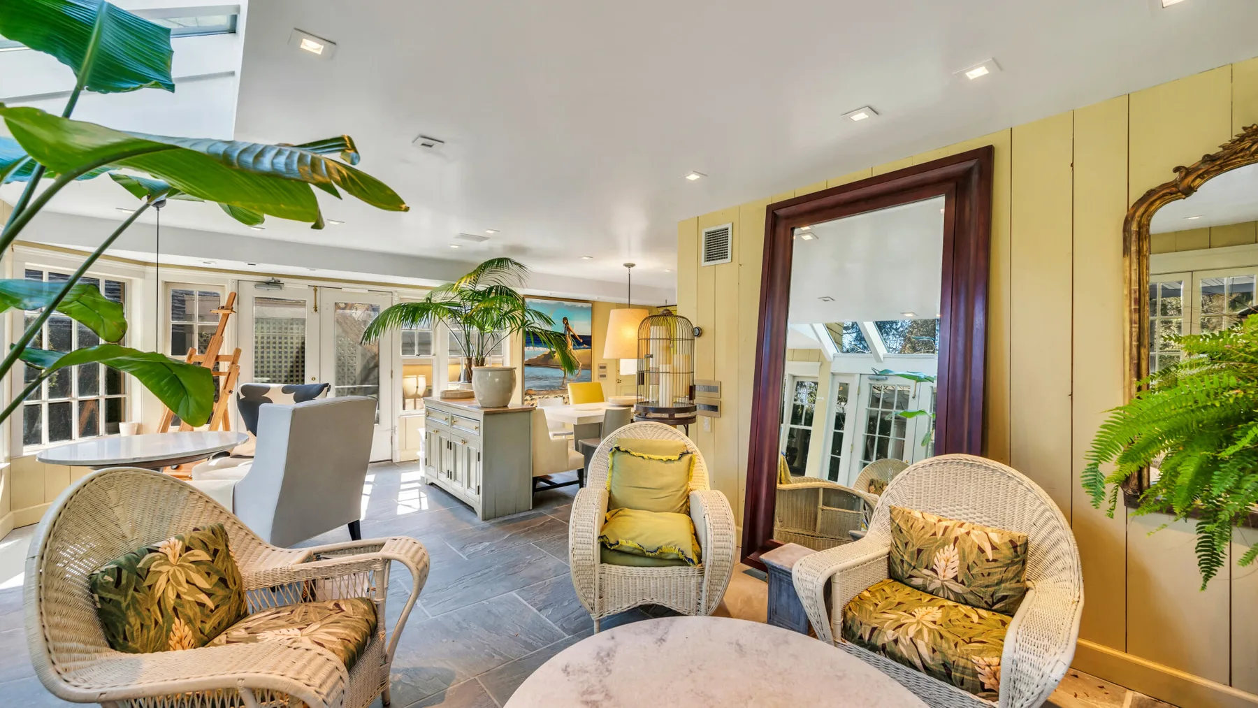 A bright lounge with woven seating, leafy plants, and an open dining area.