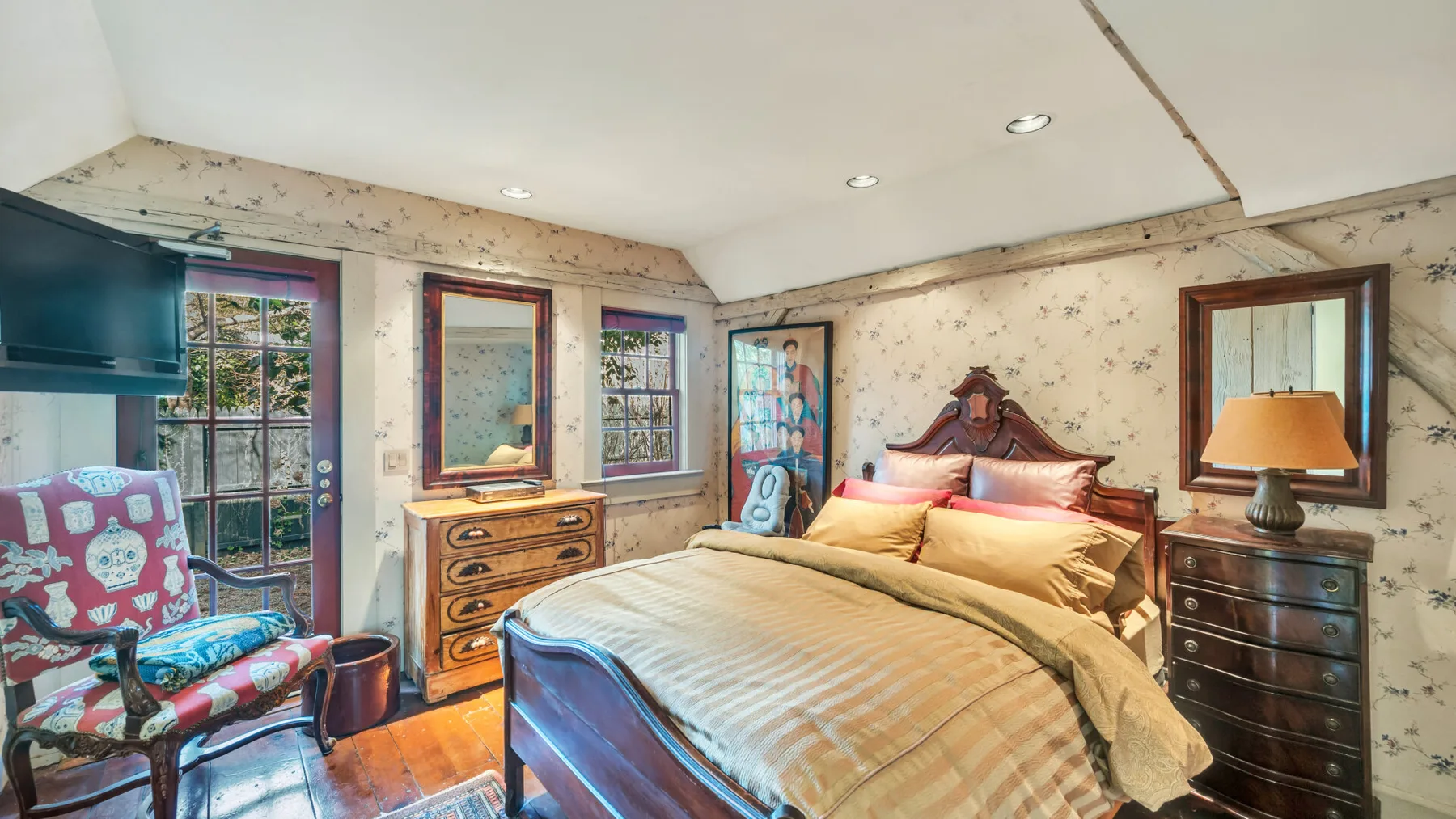 A bedroom with a large bed, wooden dressers, and a patterned armchair.