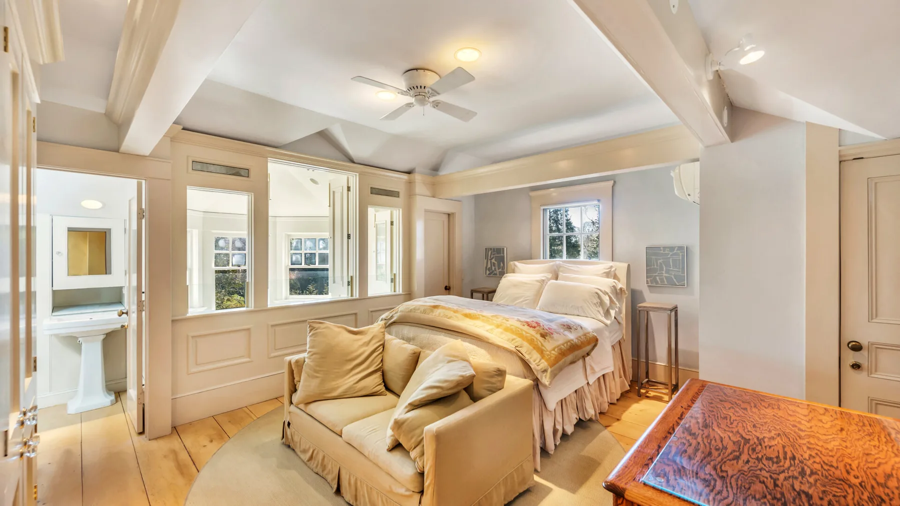 A bright bedroom with a bed, a cushioned seating area, and wood flooring.