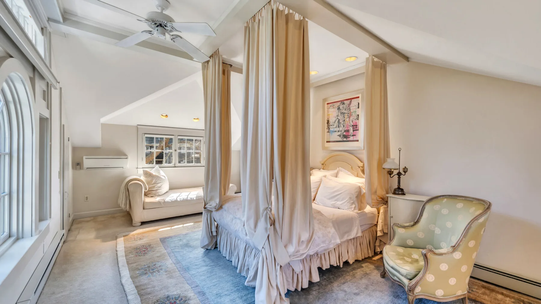 A bright bedroom with a curtained bed, a window, and an upholstered armchair.