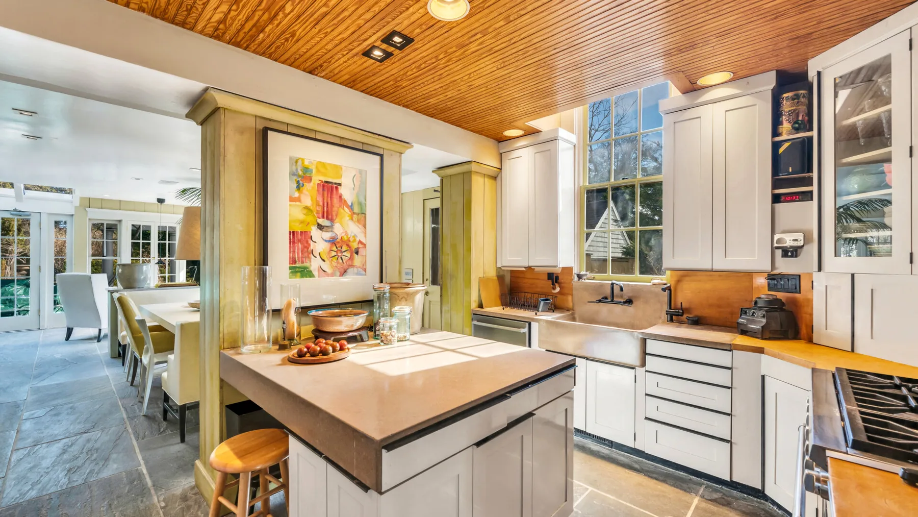 A bright kitchen with a central island, white cabinetry, and a wooden ceiling.