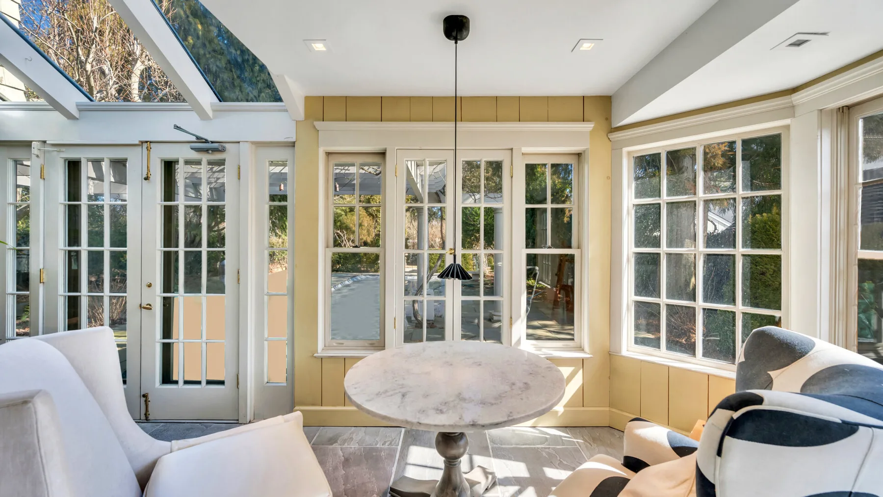A bright sunroom with large windows, glass doors, and a round table.
