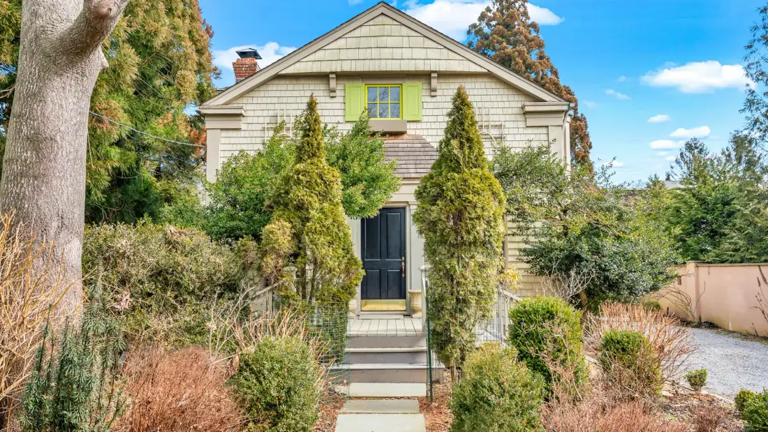 A light-colored house stands behind a garden path lined with shrubs.