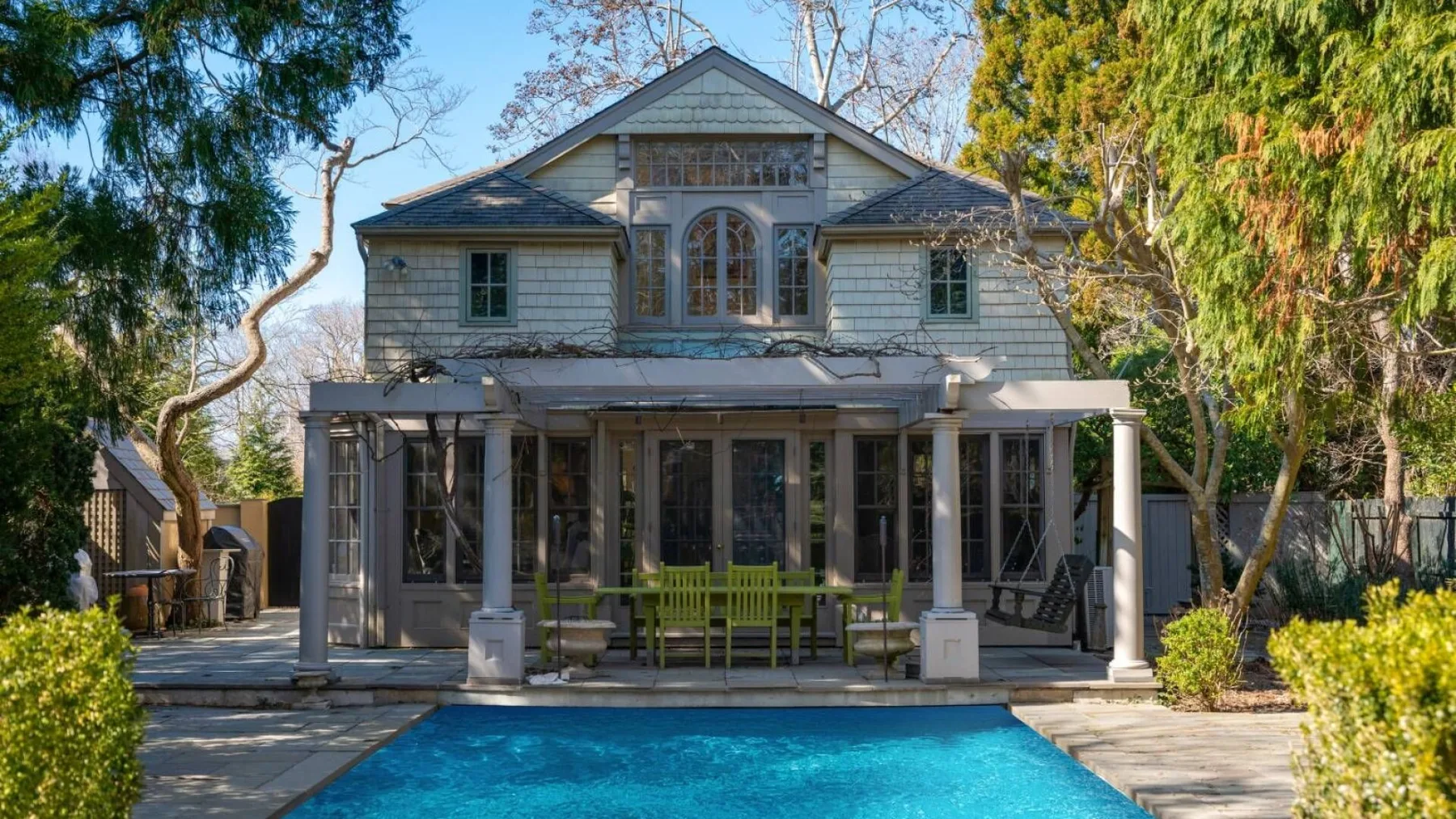 A large house with a covered patio stands behind a swimming pool.