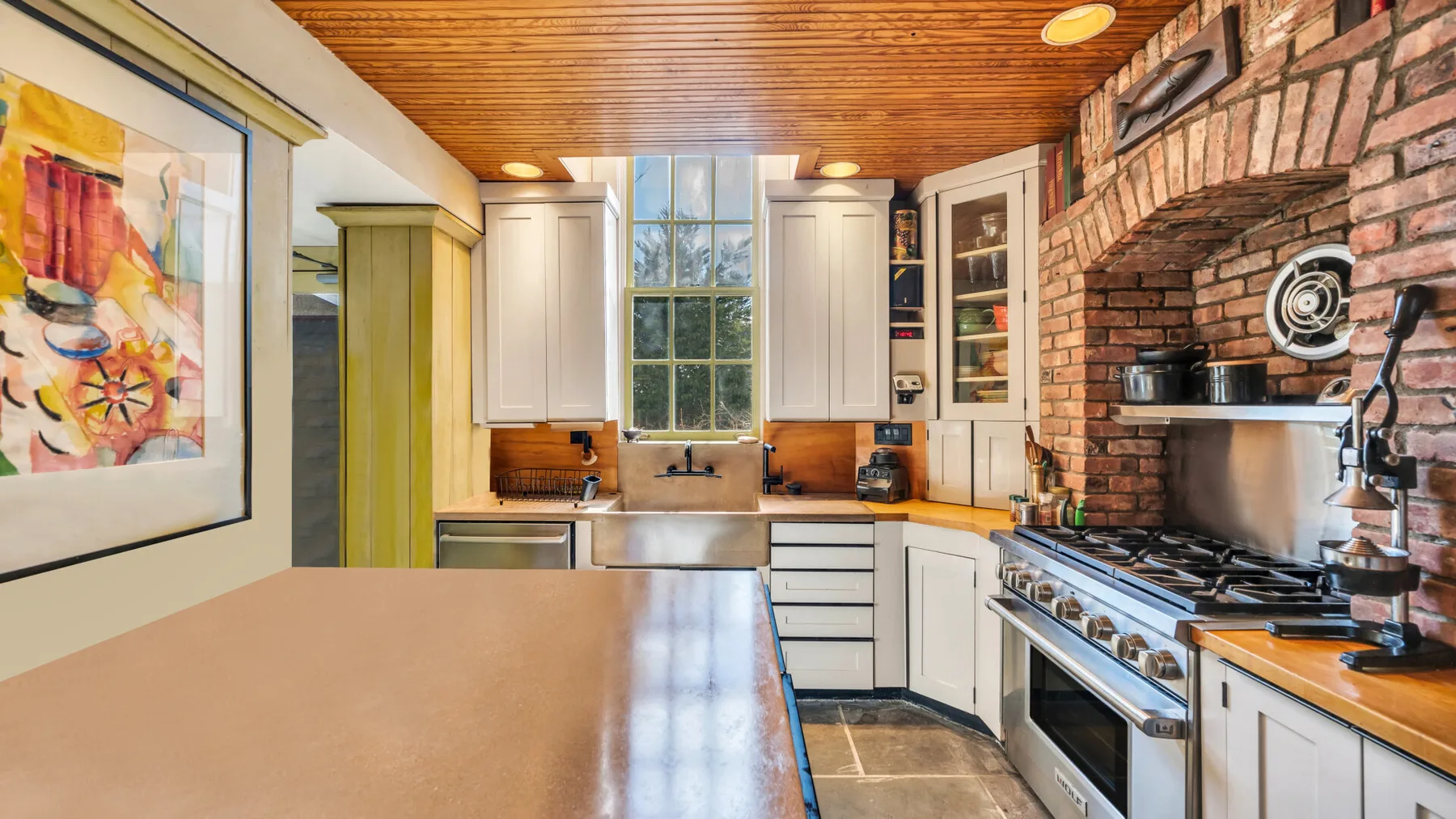 A kitchen with white cabinetry, a large range, and exposed brick walls.