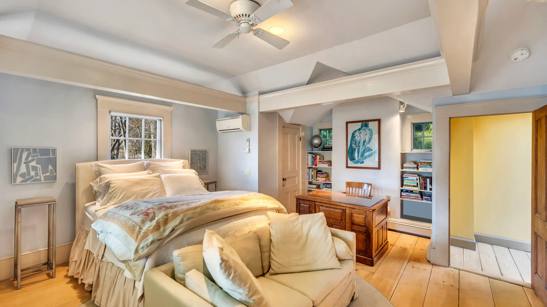 A bedroom with a bed, seating area, and wooden desk beneath a ceiling fan.