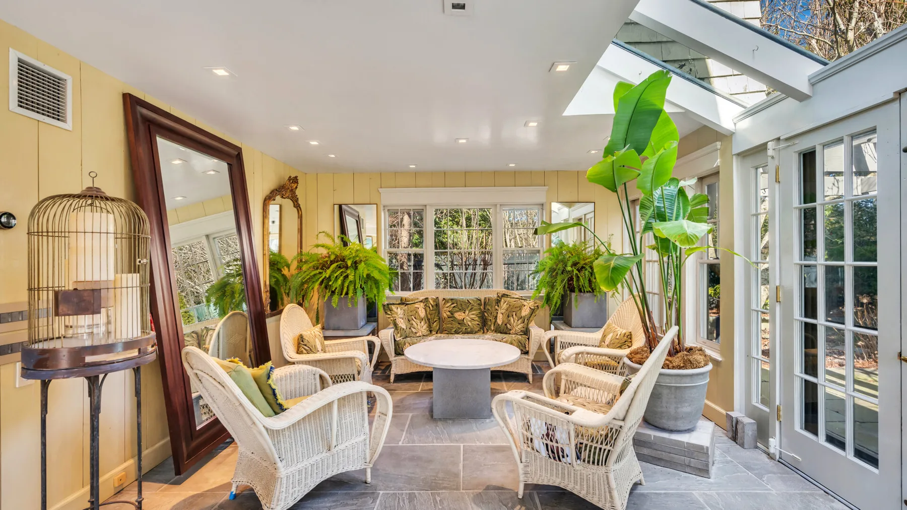 A sunroom with wicker seating, potted plants, and glass doors.