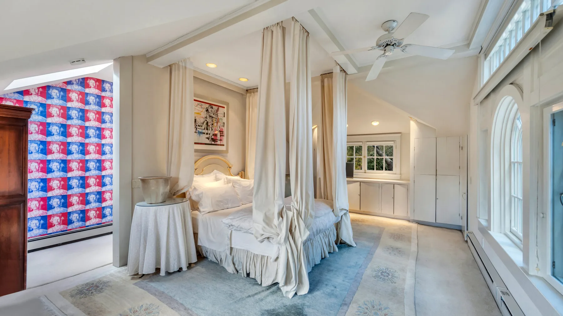 A bright bedroom with a curtained bed and large windows.