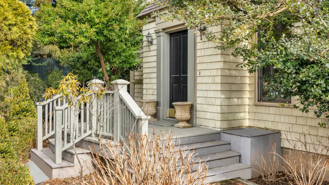 An exterior entrance with steps, a dark door, and surrounding greenery.