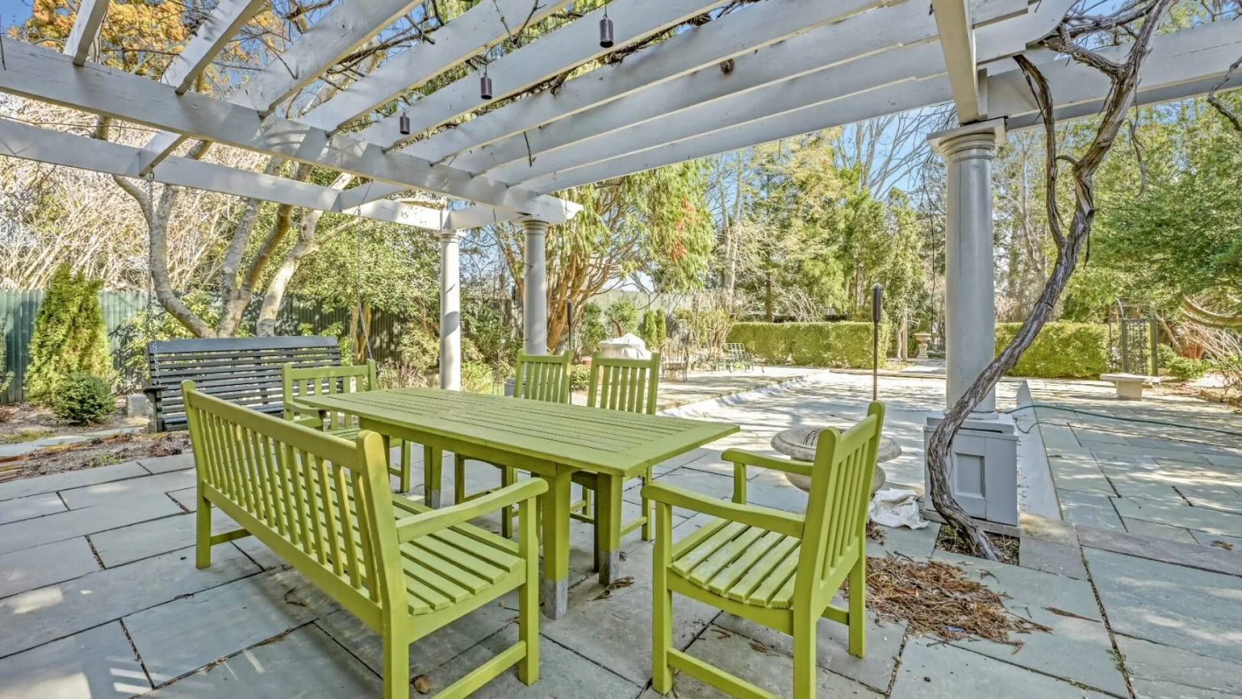 An outdoor dining area with green seating beneath a pergola.