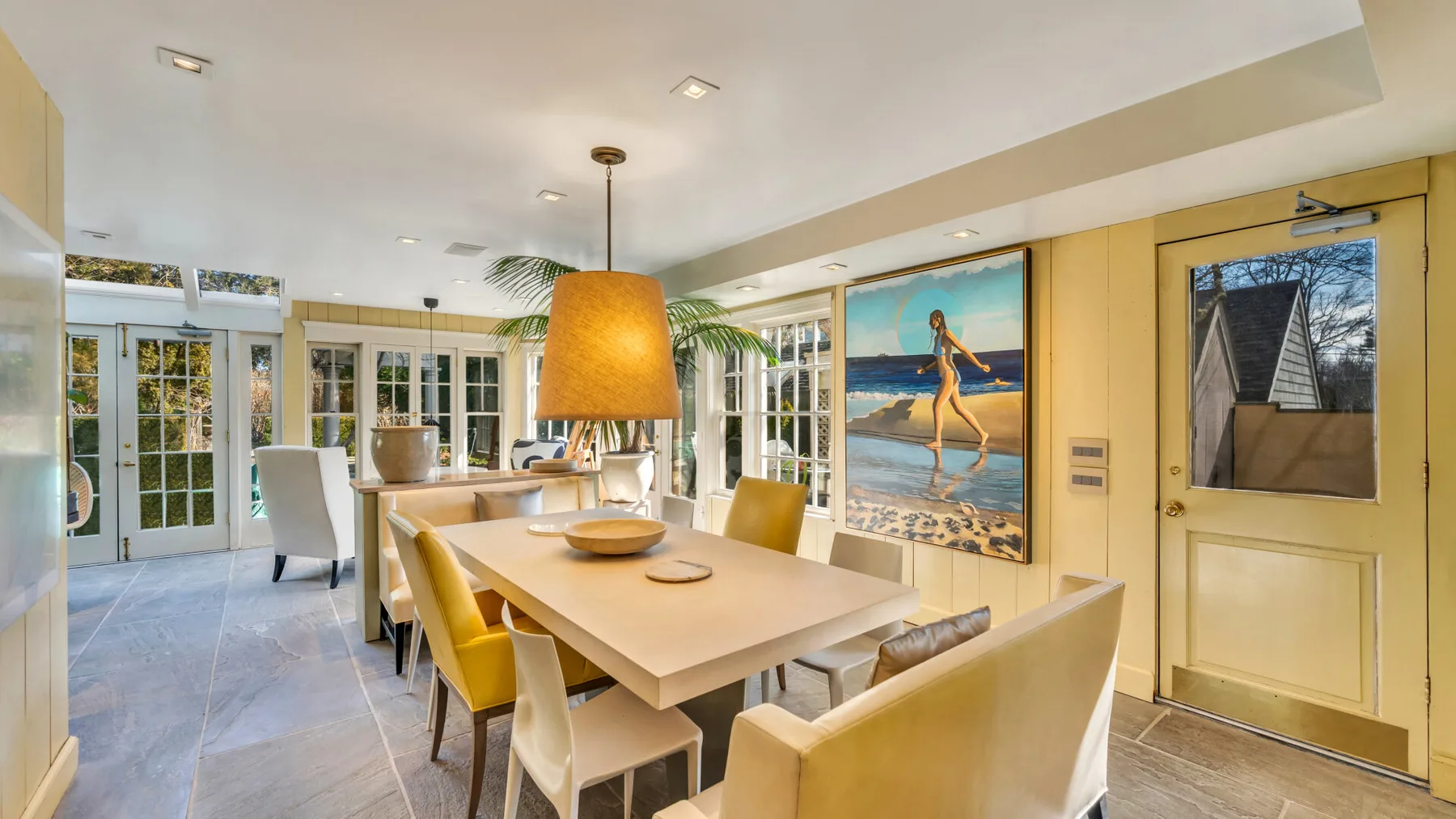 A bright dining area with a long table, pendant light, and large windows.
